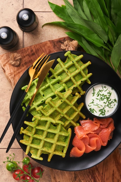 Waffles belgas verdes Espinafre ou alho selvagem ou waffles pesto com salmão vermelho e molho de creme no antigo fundo da mesa de azulejos bege Delicioso café da manhã lanche na vista superior de fundo escuro