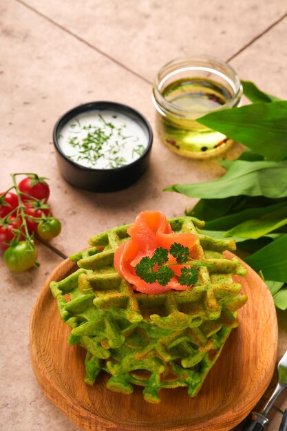 Waffles belgas verdes Espinafre ou alho selvagem ou waffles pesto com salmão vermelho e molho de creme no antigo fundo da mesa de azulejos bege Delicioso lanche de café da manhã no antigo fundo de azulejos bege