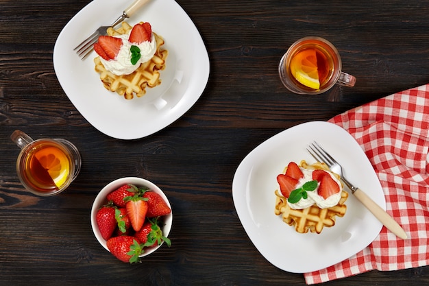 Waffles belgas vieneses decorados con crema y fresas, té y una servilleta a cuadros