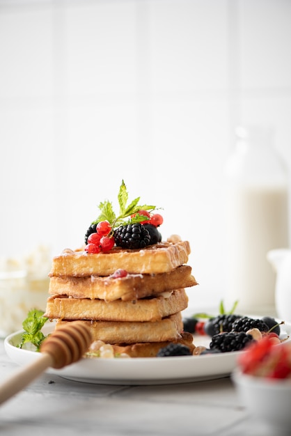 Waffles caseros con bayas y miel en una placa blanca.