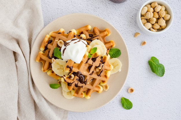 Waffles com banana fresca, avelãs, calda de chocolate e chantilly em um prato