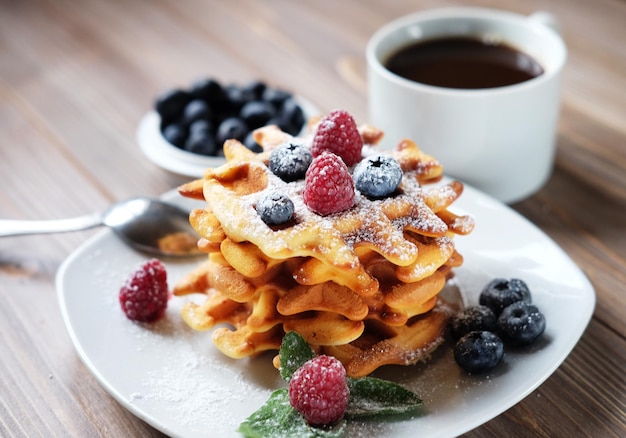 Waffles com frutas em um prato branco e café close-up