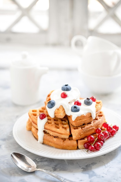 Waffles com groselhas de mirtilos derramados com iogurte em um prato de porcelana branca