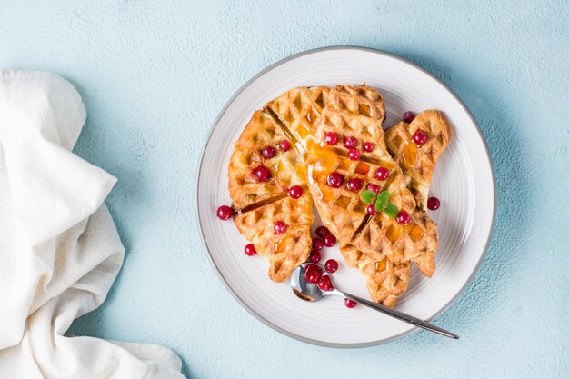 Waffles croissant crujientes con grosellas rojas, miel y menta en un plato sobre una mesa de luz. Desayuno dulce y delicioso - croffles. Vista superior