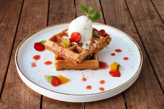 Waffles da Bélgica com frutas e sorvete Servido com prato na mesa de madeira Imagem de foco seletivo