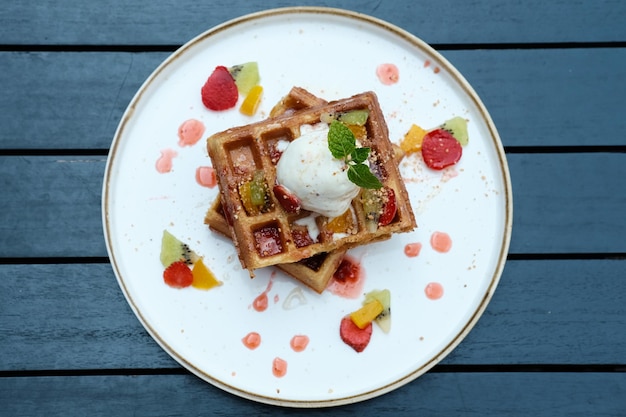 Foto waffles da bélgica com frutas e sorvete servido com prato na mesa de madeira imagem de foco seletivo