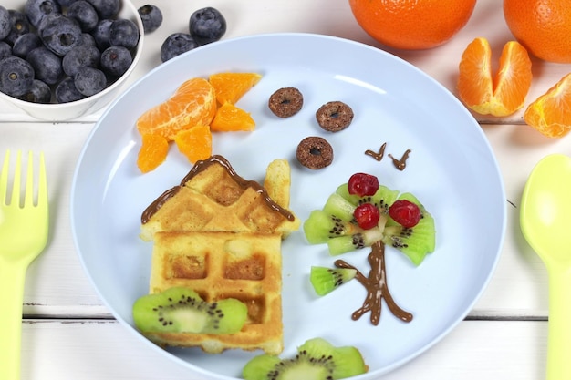 Waffles de café da manhã infantil e frutas em um prato azul Uma ideia criativa para uma divertida sobremesa ou café da manhã para crianças