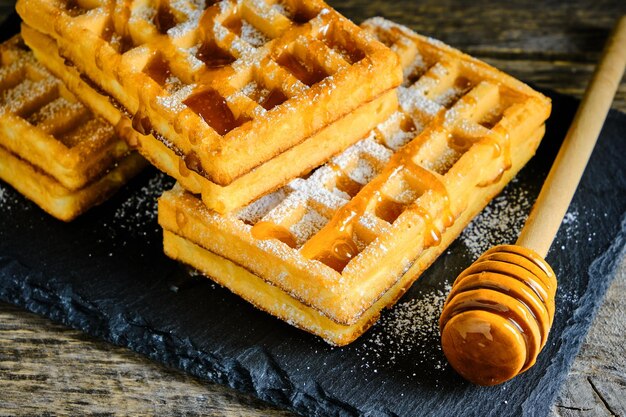 Waffles doces regados com mel e polvilhados com açúcar de confeiteiro em uma lousa