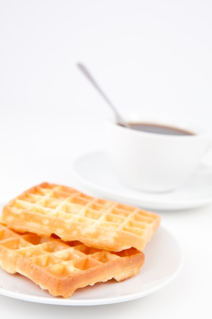 Waffles e uma xícara de café com uma colher em pratos brancos