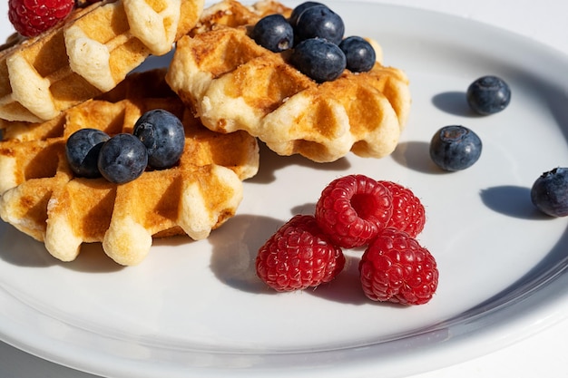 Waffles con frambuesas y arándanos en un plato de postre para el desayuno