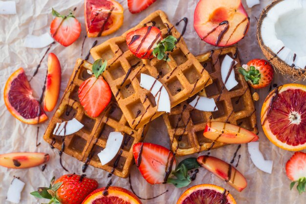 Waffles con fresas, coco, ciruela y naranja con chocolate.