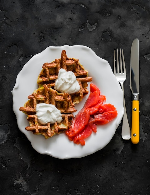 Waffles de patatas Zucchini con salmón ligeramente salado y crema fresca en un fondo oscuro vista superior