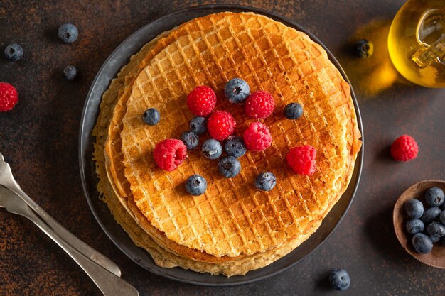 Waffles redondos crocantes dourados servidos no prato com frutas vermelhas. Fechar-se.