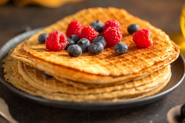 Waffles redondos crocantes dourados servidos no prato com frutas vermelhas. Fechar-se.