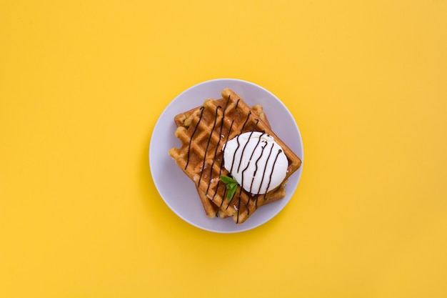 Foto waffles con salsa de chocolate, helado y menta en vista de tabla amarilla