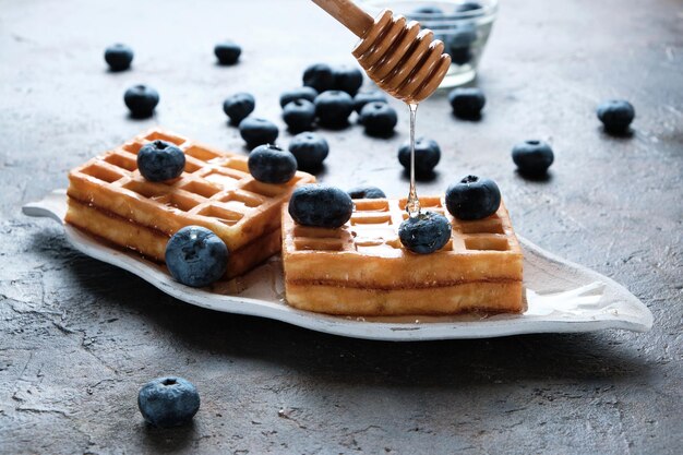 Waffles são colocados no prato, decorados com mirtilos, regados com mel da colher de mel.