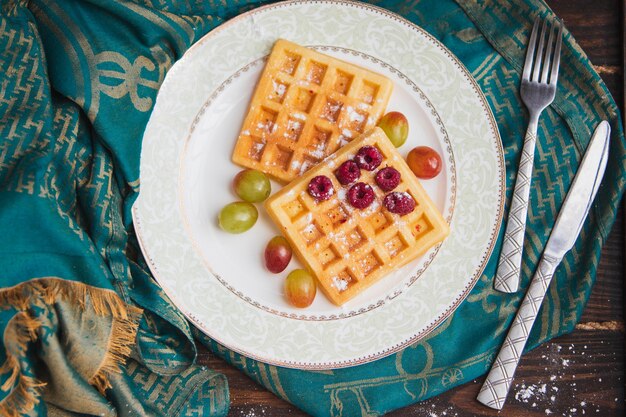 Waffles servidos con frutas, frambuesas y cubiertos