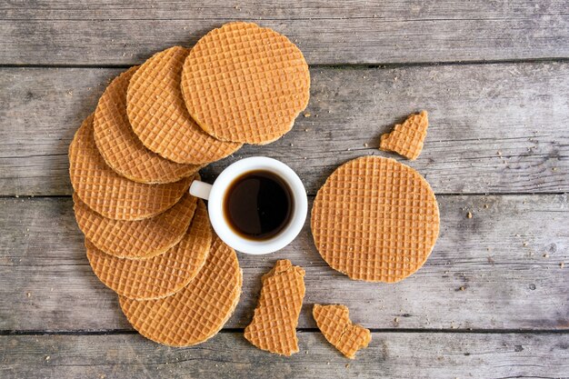 Waffles tradicionales de Holanda con caramelo y taza de café en el fondo de madera, vista superior.