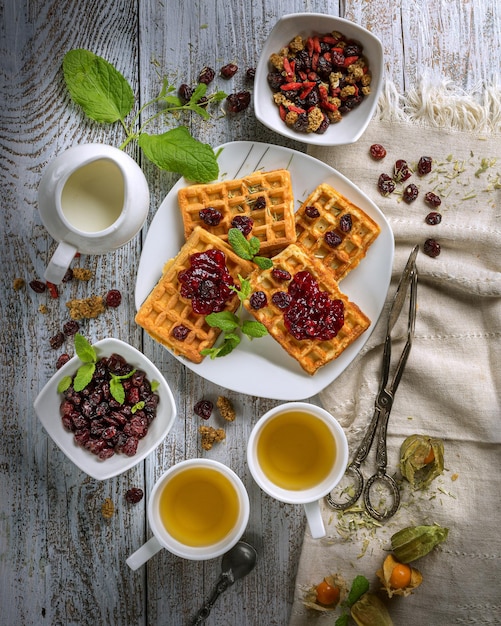Waffles vienenses com frutas e marmelada com folhas de hortelã em um prato branco sobre uma mesa de madeira clara