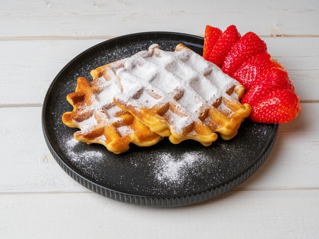 Waffles vieneses belgas recién horneados espolvoreados con azúcar en polvo con fresas