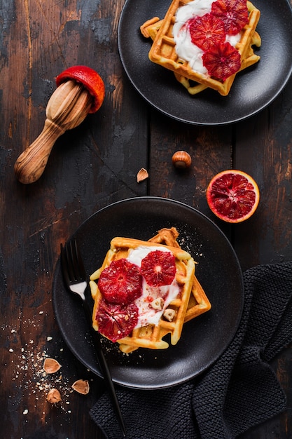 Waffles con yogur y salsa roja de naranja siciliana sobre la vieja superficie de madera oscura. Vista superior.