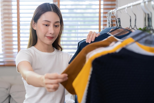 Wahl der Kleidung Nichts zum Anziehen Attraktive asiatische junge Frau Mädchen probieren appare glückliche Frau aus, die Kleid-Outfit auf Kleiderbügel im Kleiderschrank im Zimmerschrank zu Hause auswählt Entscheiden, was man anziehen soll