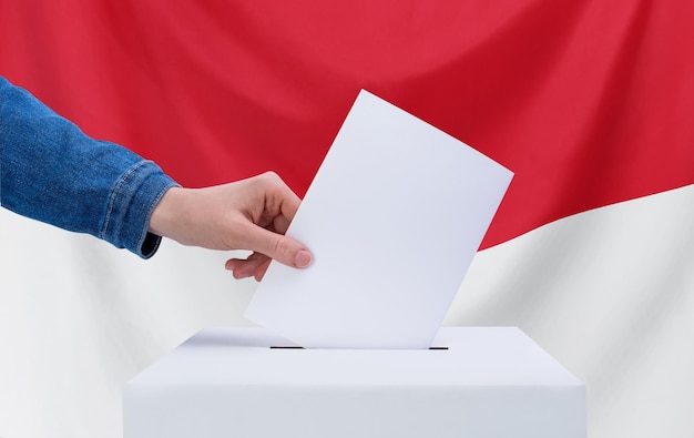 Wahlkonzept Eine Hand wirft einen Stimmzettel in die Wahlurne Indonesiens Flagge im Hintergrund