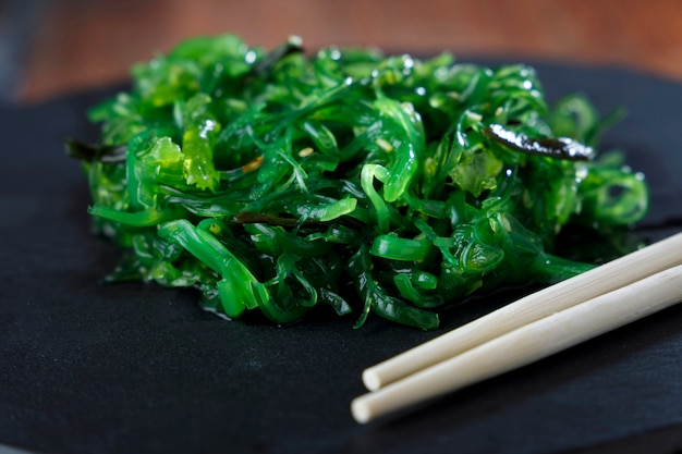 Wakame Algensalat mit Sesam auf schwarzem Teller und Holztisch