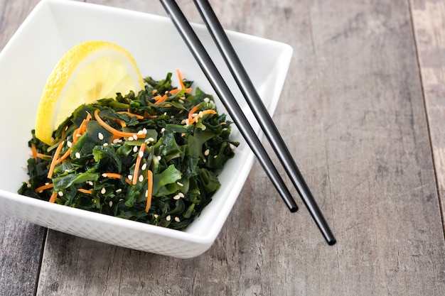 Wakame-Salat mit Karotte, Samen des indischen Sesams und Zitronensaft in der Schüssel auf Holztisch