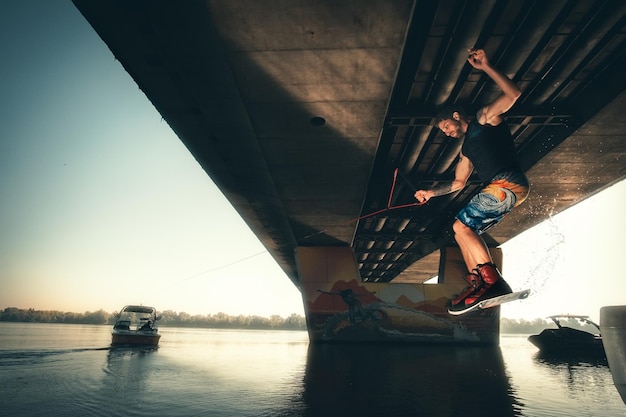 Wakeboarding, wakeboarder saltando detrás del barco con wakeboard, acción bajo el puente