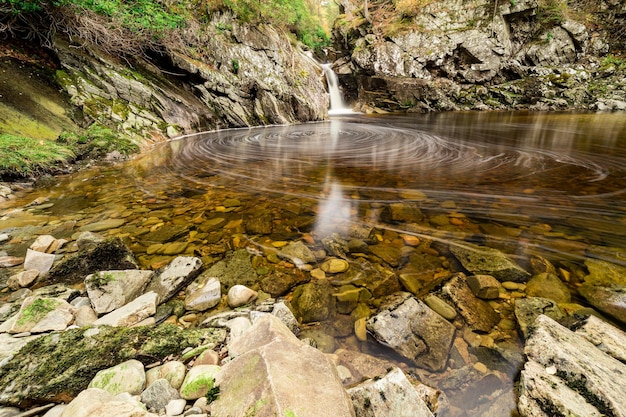 Wald in Schottland Blick auf einen kleinen Waldfluss, der einen steilen Hang hinunterfließt