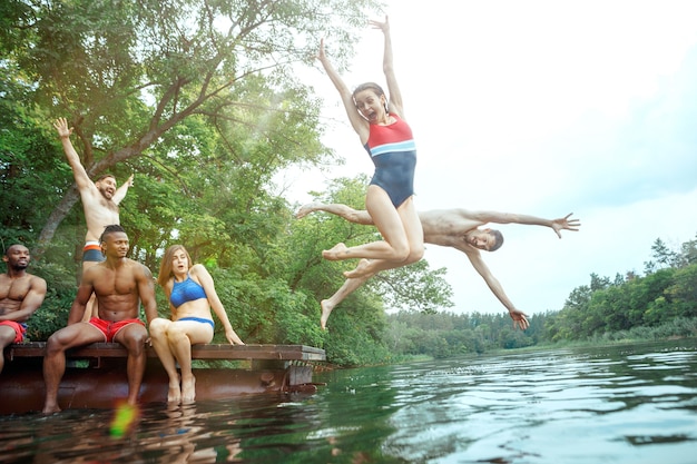 Waldparty mit Freunden genießen. Gruppe schöne glückliche junge Männer und Mädchen, die zusammen am Fluss schwimmen. Sommer, Party, Abenteuer, Jugend, Freundschaftskonzept