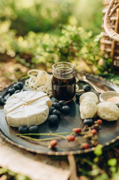 Waldpicknick auf dem Hintergrund von Moos und Heidelbeersträuchern, Käse und Beeren auf einer Metallplatte