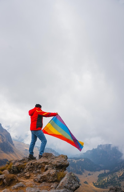 Wanderer, der eine Regenbogen-lgbt-Stolzflagge im Hochgebirge schwenkt. Inklusive SportJunger Mann beim Wandern in den Bergen