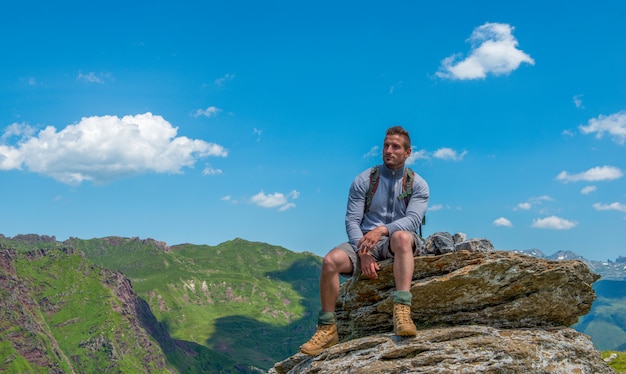 Wanderer des jungen Mannes, der auf einem Felsen im Berg sitzt