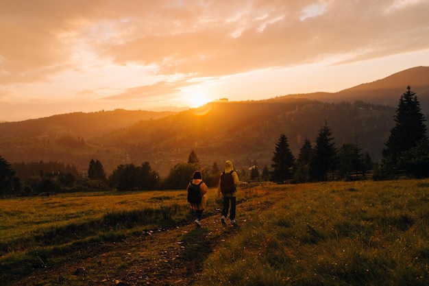 Wanderer gehen die Wiese vor dem Hintergrund des Sonnenuntergangs in der Regen- und Berglandschaft hinunter