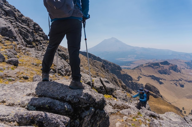 Wanderer junger Mann mit Rucksack und Trekkingstöcken, der am Rand der Klippe steht und die Berge betrachtet