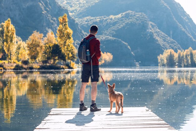 Wanderer junger Mann Reisender mit Rucksack mit seinem Hund, der die Landschaft im See betrachtet.