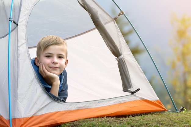 Wanderer-Kinderjunge, der in einem Zelt auf einem Bergcampingplatz sitzt und den Blick auf die Natur genießt.