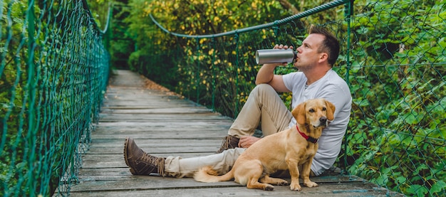 Wanderer mit dem Hund, der auf hölzerner Hängebrücke stillsteht