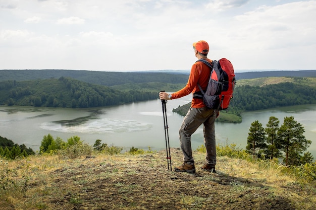 Wanderer mit Rucksack entspannt sich auf einem Hügel und genießt die Aussicht auf das Tal mit Bergen und See