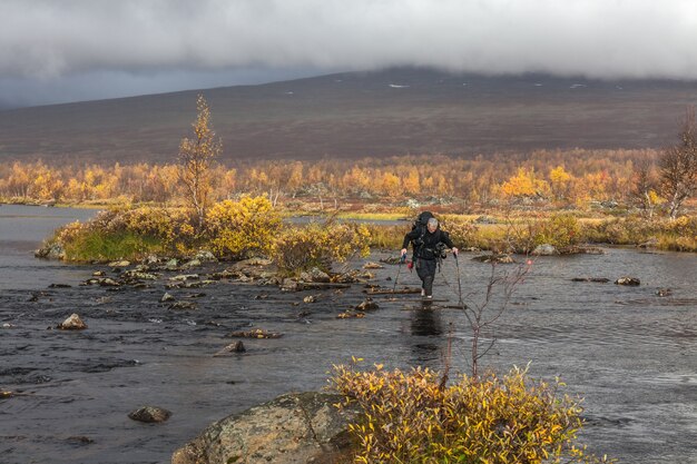 Wanderer mit Rucksack überquert Cold Creek. auf einer Trekkingtour in Sarek