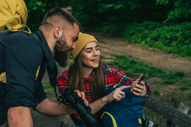 Wanderer sitzen auf einer Bank im Wald und machen mit einem Smartphone eine Pause