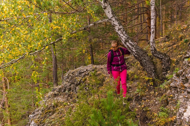 Wandererin mit Rucksack geht vorsichtig auf einem Bergpfad durch den Herbstwald