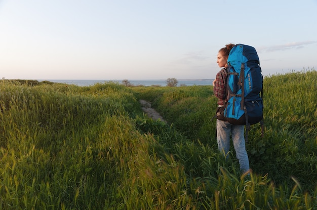 Wanderermädchen reist mit einem Rucksack auf dem Landschaftshintergrund