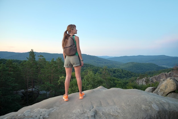 Wanderfrau, die auf einem Bergwanderweg steht und die abendliche Natur während ihrer Reise auf dem Wildnispfad genießt Einsame weibliche Reisende, die eine hohe Hügelroute durchqueren Gesundes Lebensstilkonzept