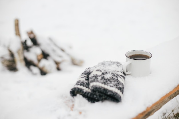 Wanderlust Quente xícara de chá e luvas de malha aconchegantes na neve no banco de madeira em Winter Park Hiking