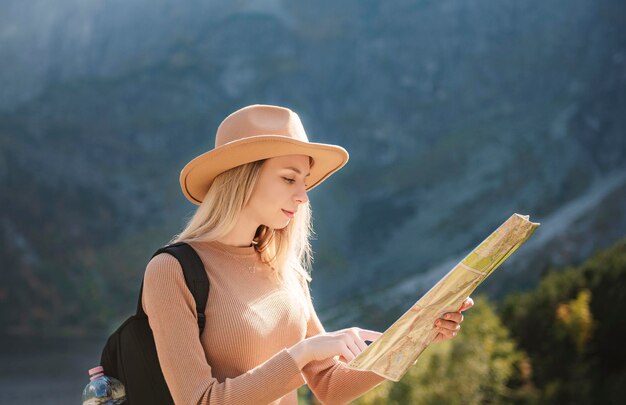 Wanderlust und Reisekonzept. Stilvolles Reisendes Mädchen mit Hut, das auf die Karte schaut und Wälder erkundet. Junger oman mit rucksack, der am see im wald reist.