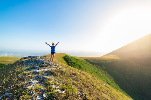 Wandern in den Bergen der Region Umbrien, Monte Cucco, Appennino, Italien. Frau mit ausgestreckten Armen in grüner Landschaft einzigartige Hügel- und Berglandschaft. Sommeraktivitäten im Freien.