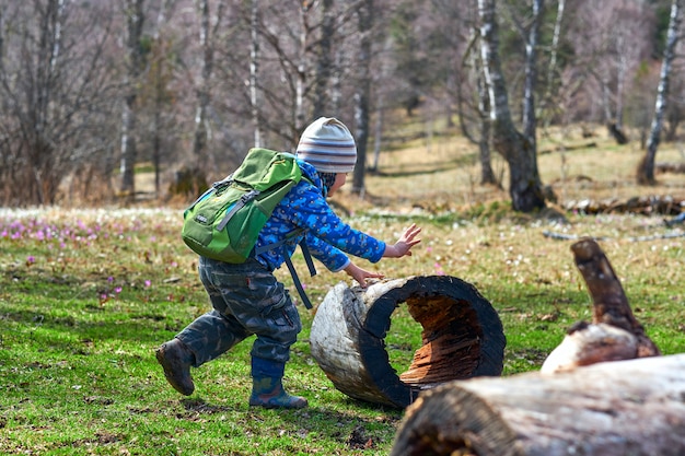 Wanderndes Kind mit Rucksäcken spielen mit einem Baumstumpf, rollen ihn wie ein Rad